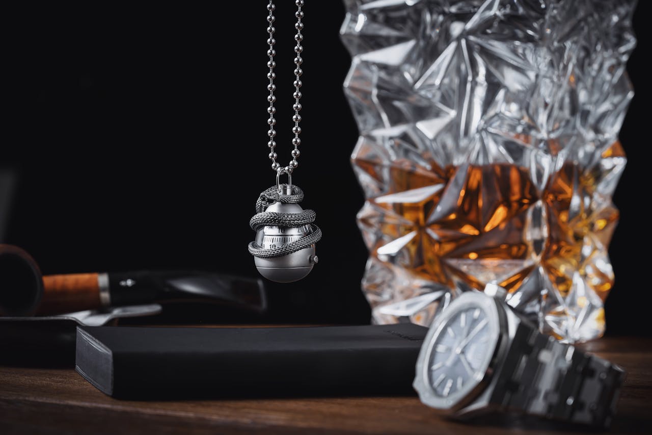 A sophisticated display of a silver necklace with snake design, paired with a wristwatch and decanter.